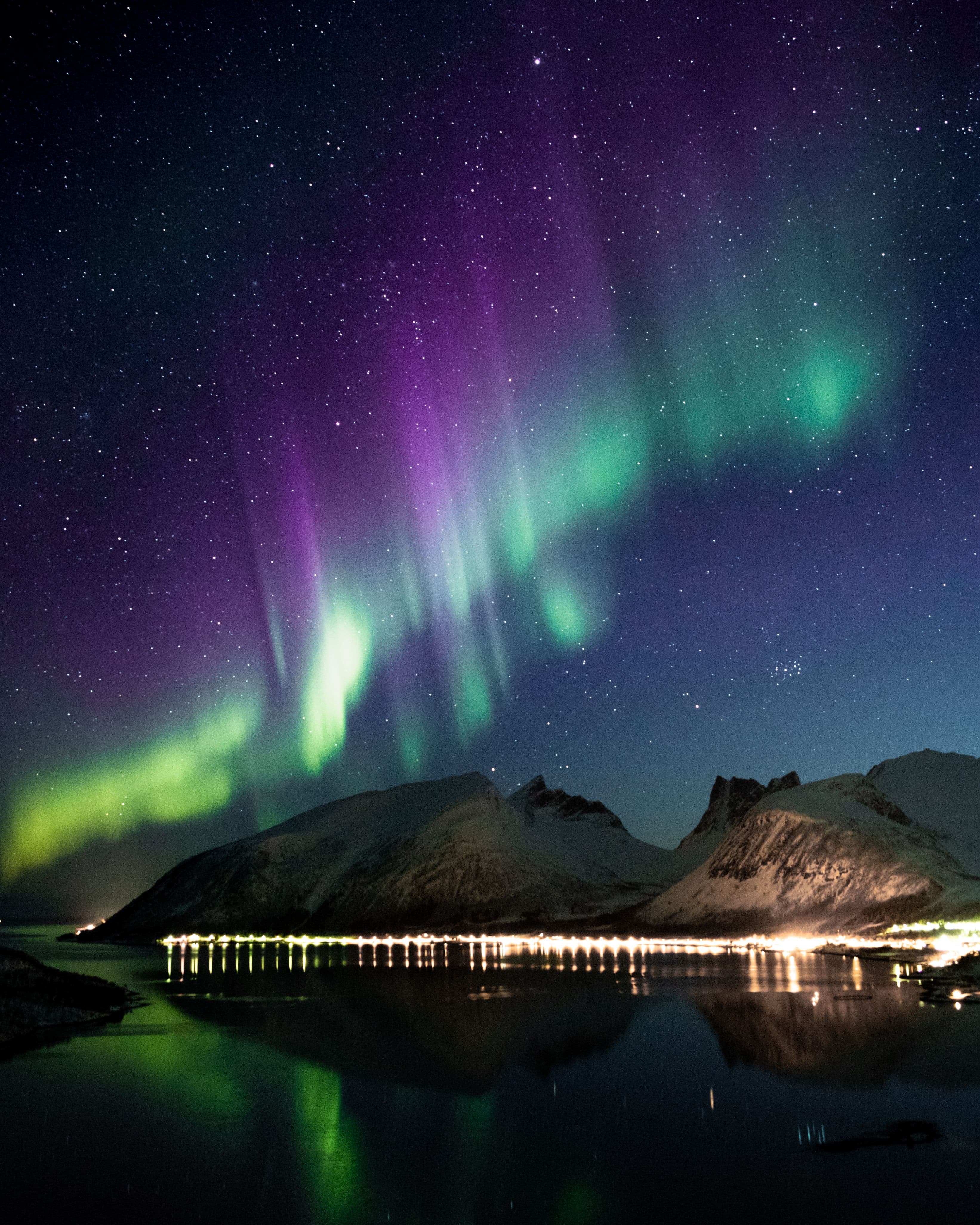 Aurora borealis above snow-covered mountains reflected in water